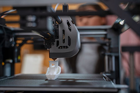 熱溶解積層法（FDM）の3Dプリンターが熱可塑性フィラメントを押出し、小型のポリマー部品を層ごとに造形している様子。