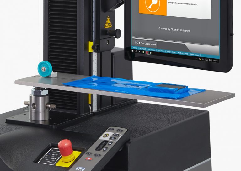 Close-up of an Instron 68SC universal testing machine with ASTM D1894 / ISO 8295 coefficient of friction fixture with a weighted sled on a blue film specimen laid across the horizontal test platform, with Bluehill Universal software visible on the operator dashboard.